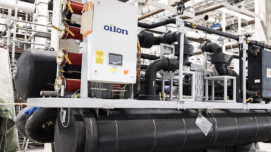 Industrial refrigeration or heat pump system with large black insulated pipes and an Oilon control unit installed in a mechanical plant room.