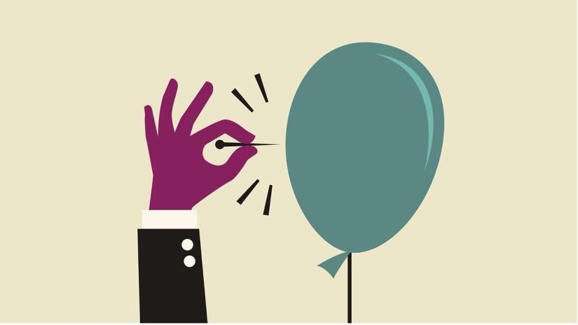 A hand holds a pin that's about to pop a balloon. 