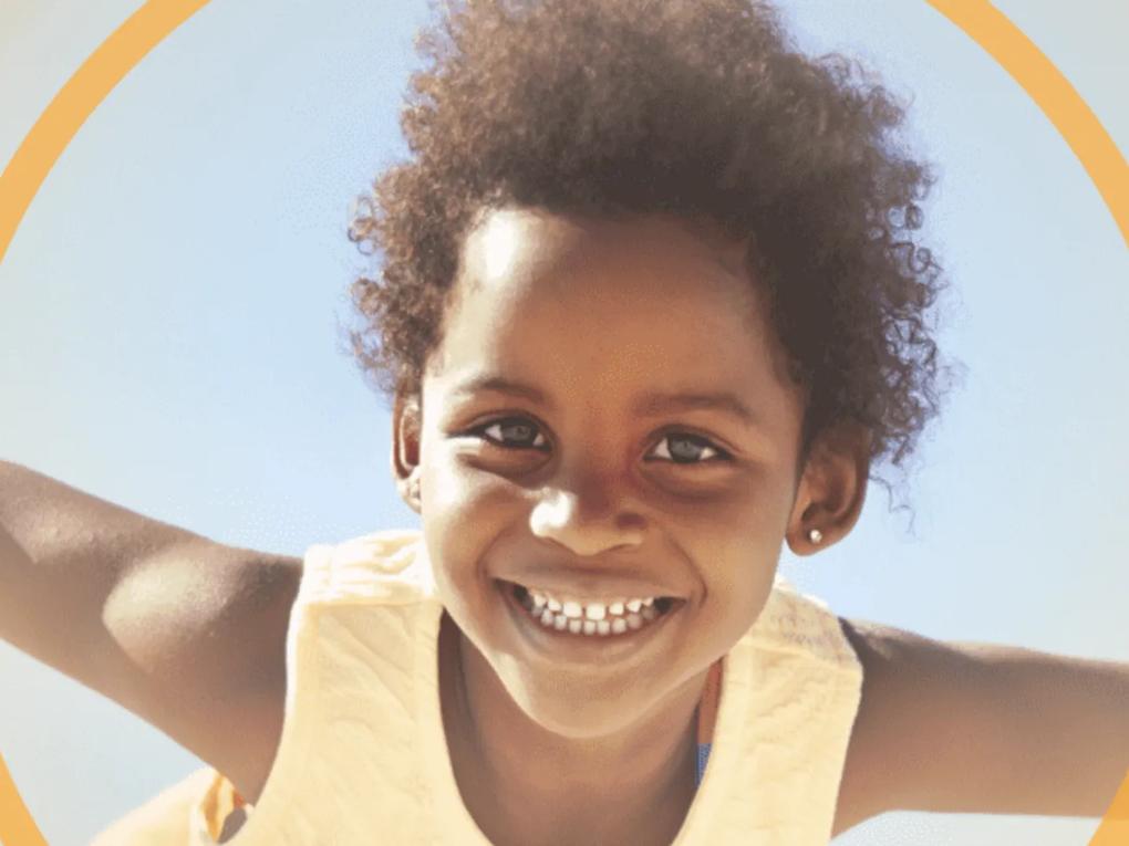 A smiling child with curly hair against a clear blue sky.