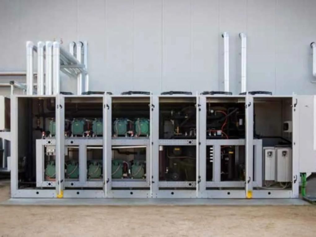 An industrial refrigeration unit with multiple compartments and visible piping, set against a plain wall.