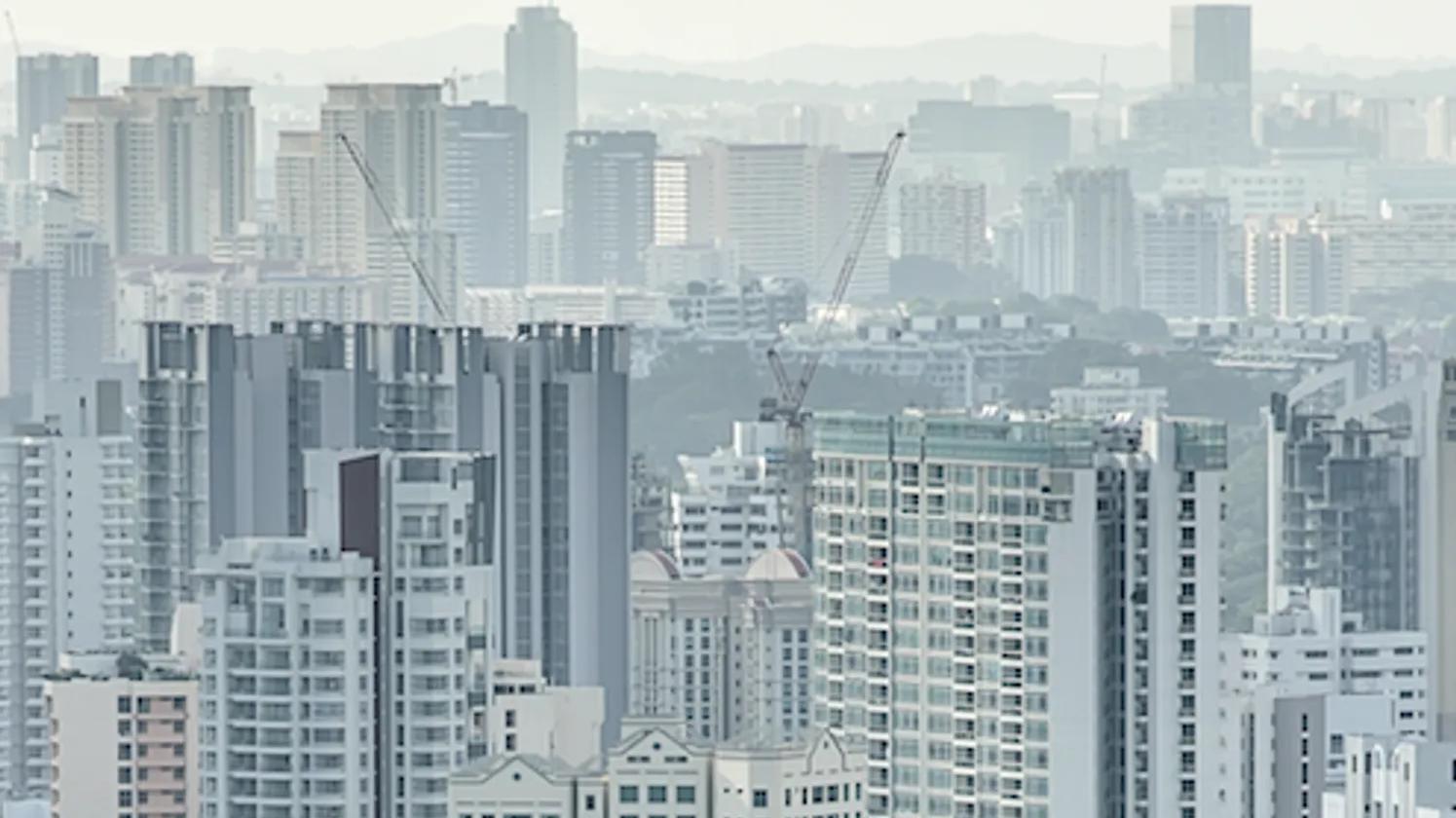A cityscape with numerous high-rise buildings and construction cranes, set against a hazy background.