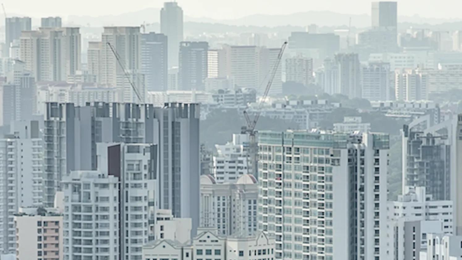 A cityscape with numerous high-rise buildings and construction cranes, set against a hazy background.