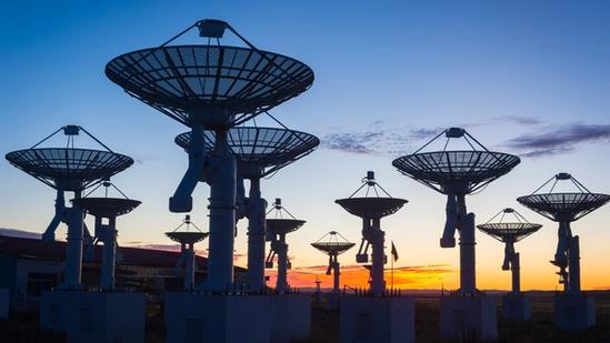 Array of large satellite dishes silhouetted against a colorful sunset sky.
