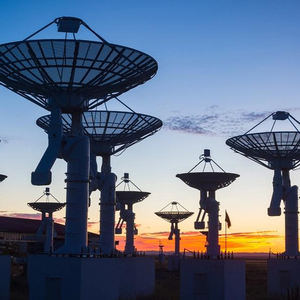 Array of large satellite dishes silhouetted against a colorful sunset sky.