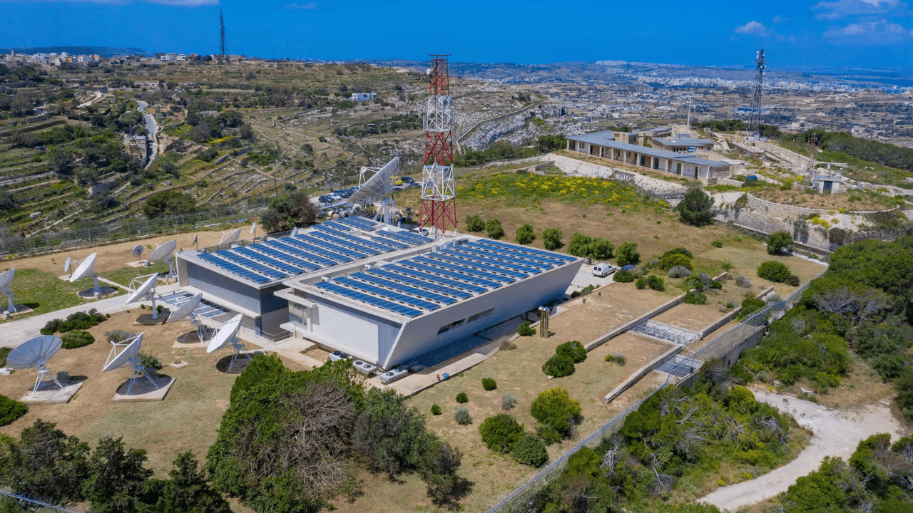 Aerial view of a satellite communication facility, set in a rural landscape with hills and scattered buildings.
