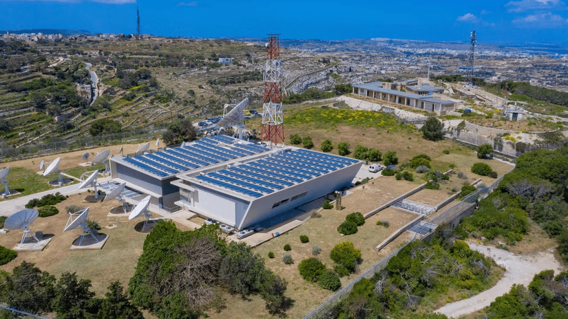 Aerial view of a satellite communication facility, set in a rural landscape with hills and scattered buildings.