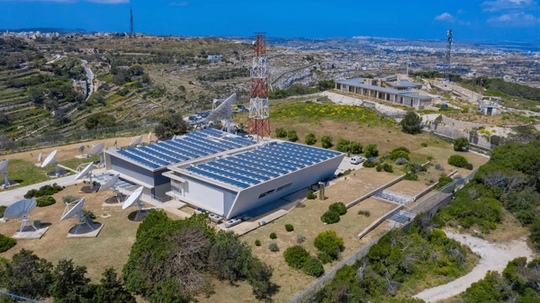 Aerial view of a satellite communication facility, set in a rural landscape with hills and scattered buildings.