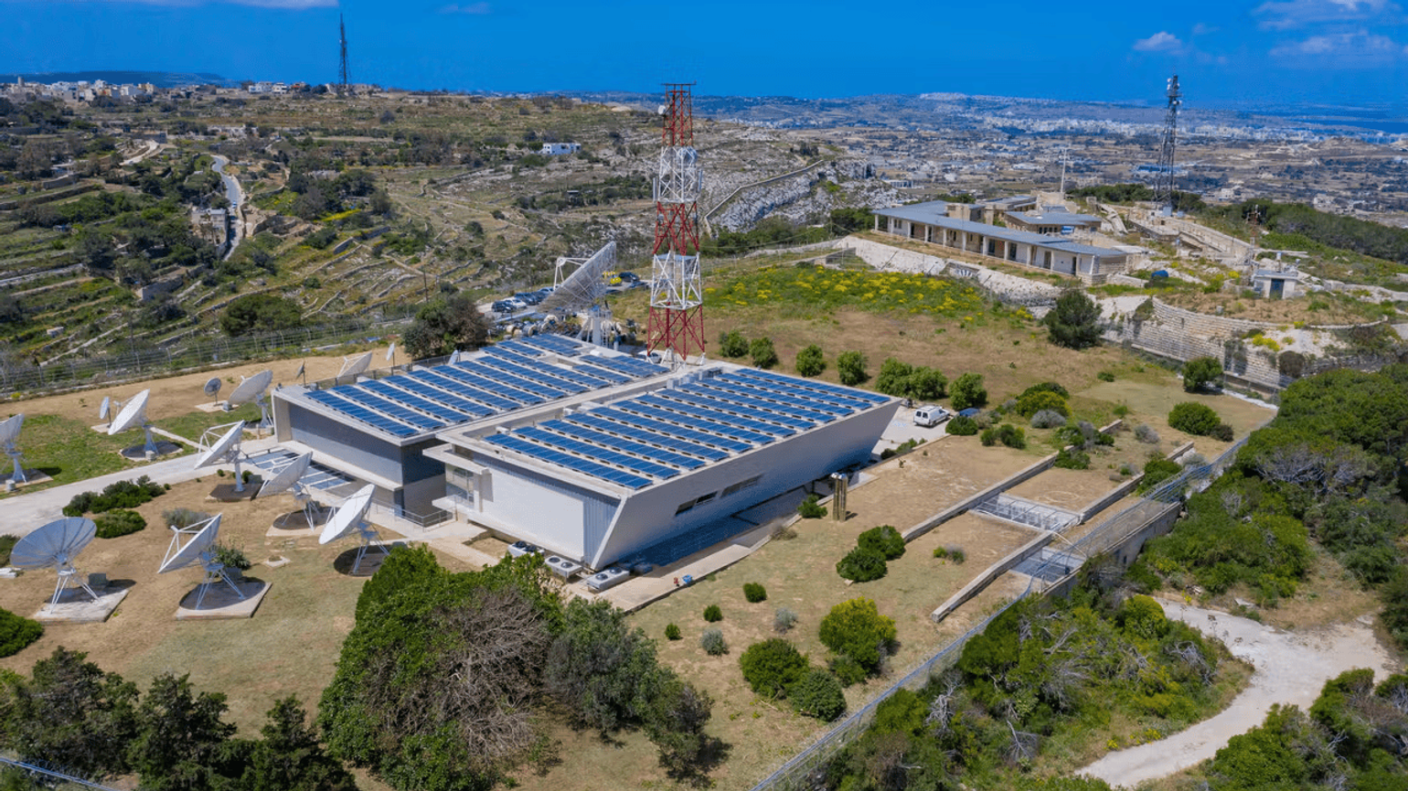 Aerial view of a satellite communication facility, set in a rural landscape with hills and scattered buildings.