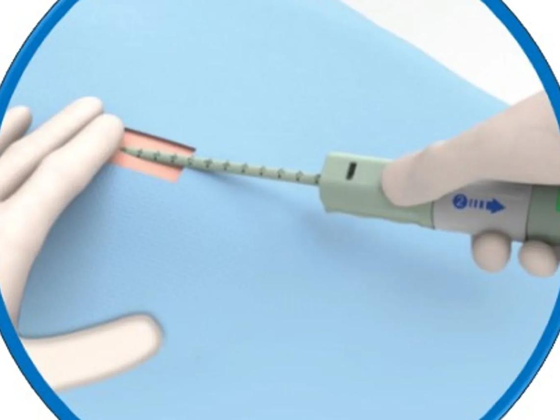 gloved hand using a medical device to make an incision on a blue surface.