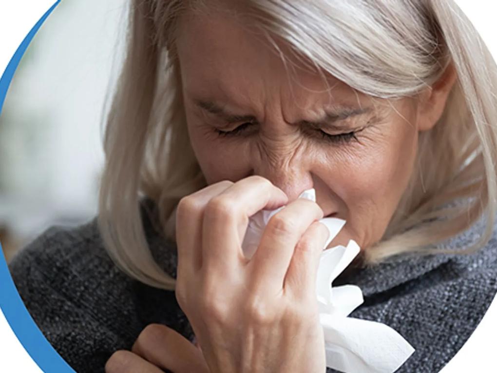 A woman with blonde hair sneezing into a tissue.