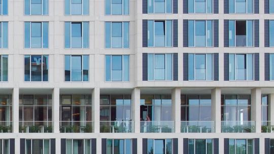 A modern building facade with large glass windows and balconies, featuring a symmetrical design and a light-colored exterior.