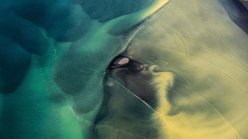 Aerial view of a river delta with swirling patterns of blue and yellow sediment in the water.