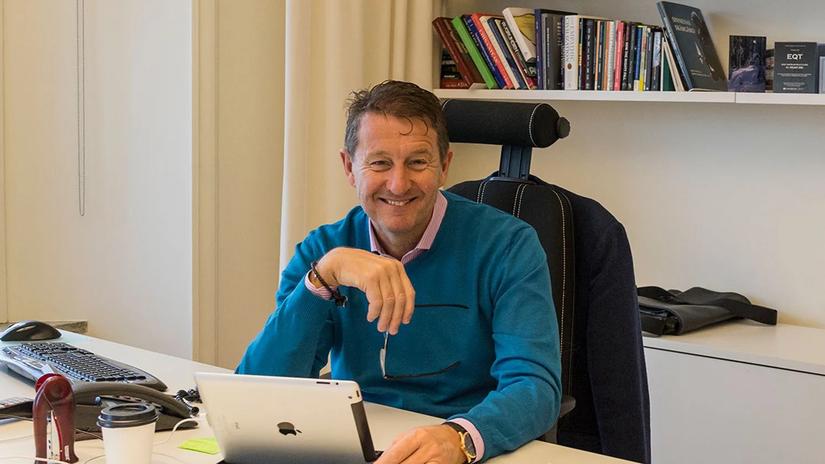 Conni Jonsson sitting at a desk, smiling, with a tablet in front of them. The background features a bookshelf filled with books.