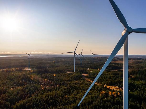 Aerial view of wind turbines scattered across a forested landscape, with the sun shining brightly in the sky.