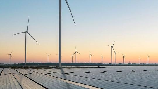 Solar panels in the foreground with multiple wind turbines stretching into the distance at sunset.