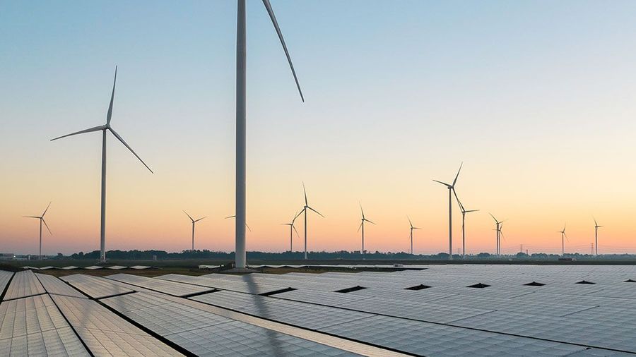 Solar panels in the foreground with multiple wind turbines stretching into the distance at sunset.