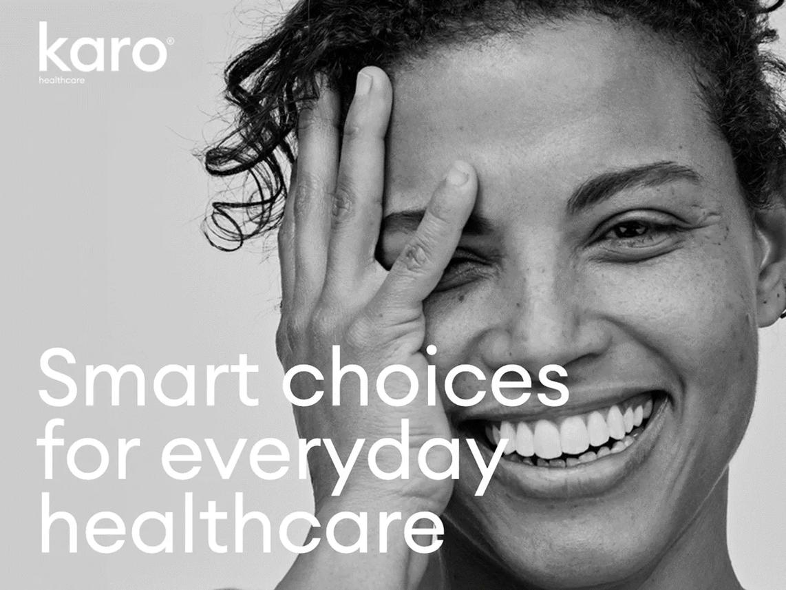 A smiling person with curly hair covers one eye with their hand.