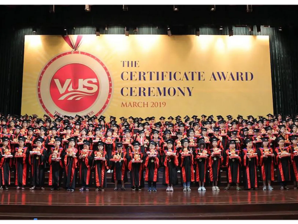 A large group of graduates in caps and gowns stand on stage holding certificates.