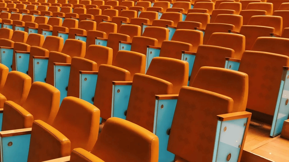 Rows of empty orange auditorium seats with blue side panels.