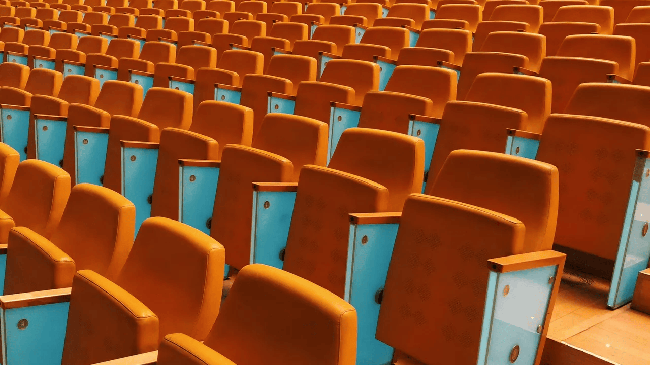 Rows of empty orange auditorium seats with blue side panels.