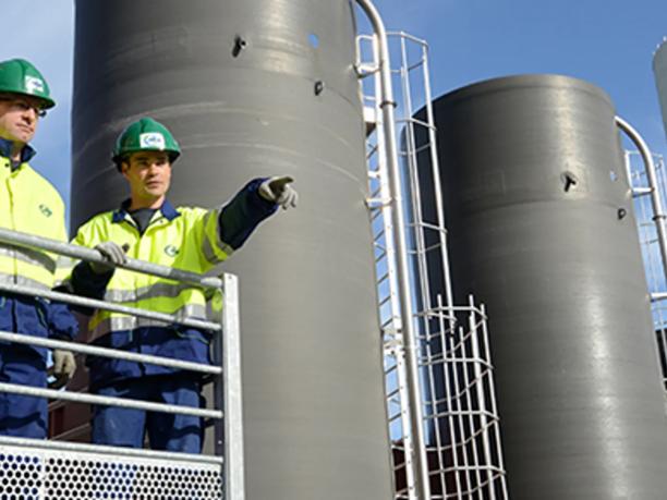 Two workers in high-visibility jackets and green hard hats stand on a platform.