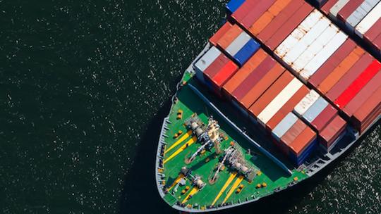 Aerial view of a cargo ship loaded with colorful shipping containers, sailing on dark water.