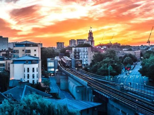 A cityscape at sunset with a railway track running through the center, surrounded by buildings and trees.