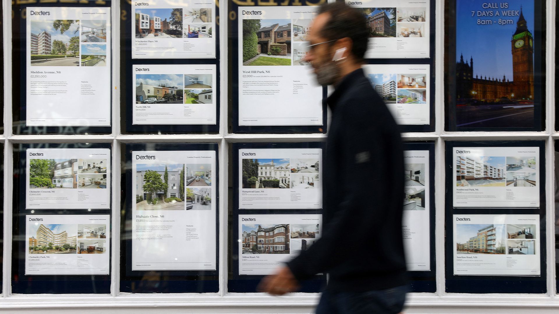 A man walks past a real estate agency window displaying property listings and photos.