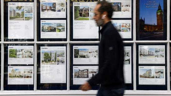 A man walks past a real estate agency window displaying property listings and photos.