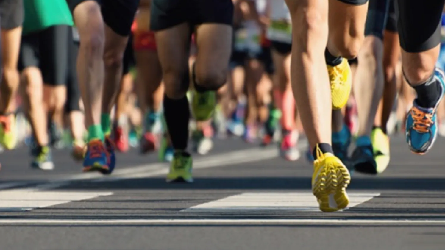 Runners in a marathon, focusing on their legs and colorful running shoes on the road.