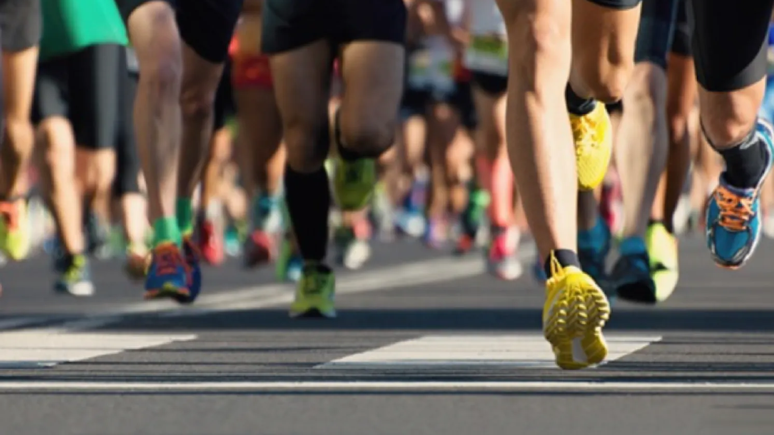 Runners in a marathon, focusing on their legs and colorful running shoes on the road.