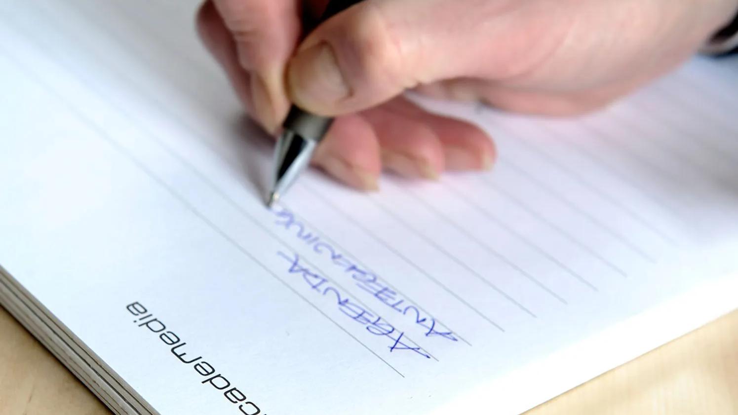 A hand writing with a pen on a lined notepad labeled "academedia," with the word "ARGENTINA" written in blue ink.