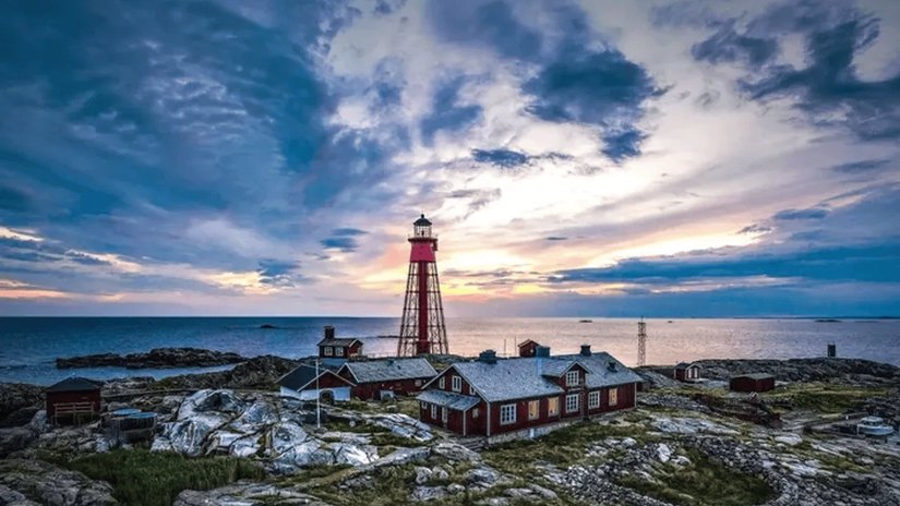 A scenic view of a coastal landscape with a red and white lighthouse and a rocky shoreline under a dramatic sky at sunset.