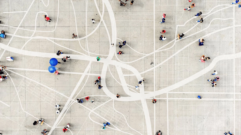 Aerial view of a large open plaza with people walking and gathering, featuring abstract white lines and patterns on the ground.