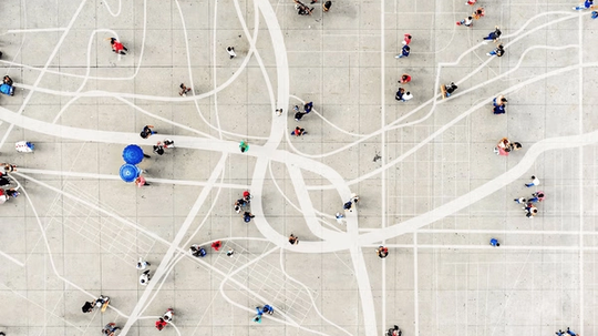 Aerial view of a large open plaza with people walking and gathering, featuring abstract white lines and patterns on the ground.