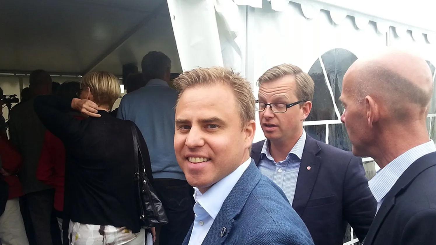 A group of people standing outside a white tent, with one person in the foreground smiling at the camera. The scene appears to be a social or professional gathering.