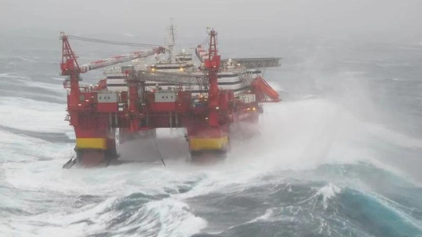 A large offshore oil platform in rough seas, with waves crashing against its structure, highlighting the challenging conditions of ocean-based operations.
