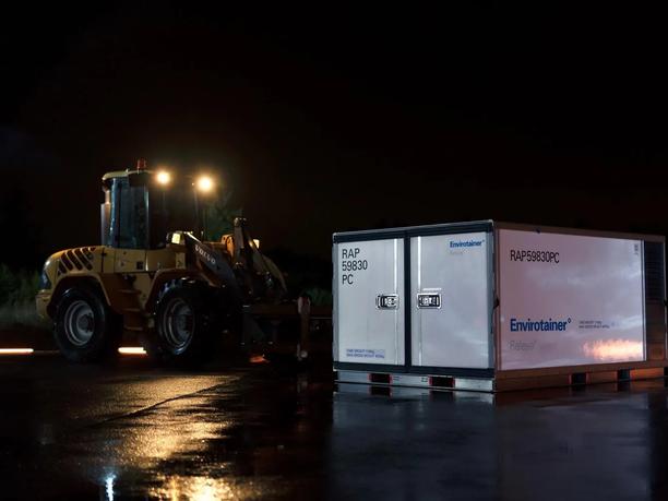 A large white Envirotainer container is positioned on a wet tarmac at night.