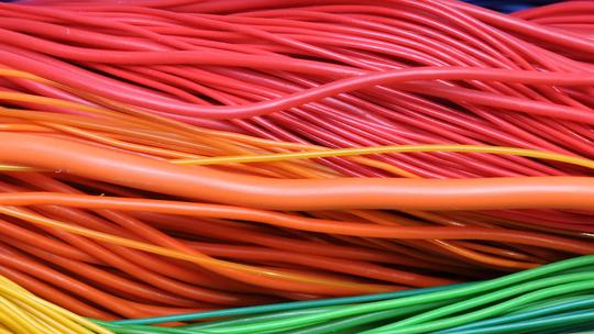 Close-up of colorful electrical wires, including red, orange, yellow, green, and blue, intertwined together.
