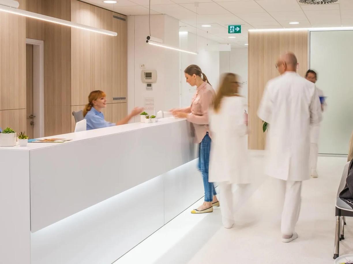 A modern medical reception area with two receptionists in blue uniforms behind a white desk.