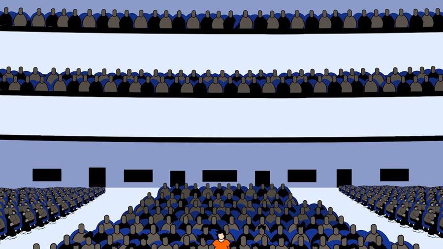 A figure in an orange shirt sits among many figures wearing dark clothes.