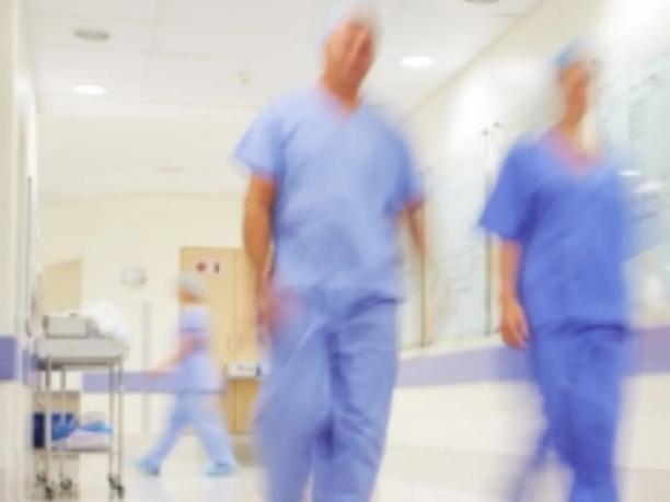 Blurred image of medical professionals in blue scrubs walking down a hospital corridor.