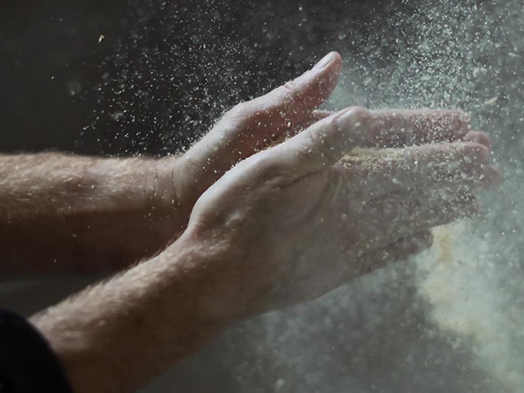 Hands clapping together, creating a cloud of flour or dust particles in the air.