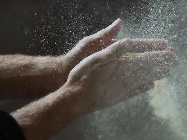 Hands clapping together, creating a cloud of flour or dust particles in the air.