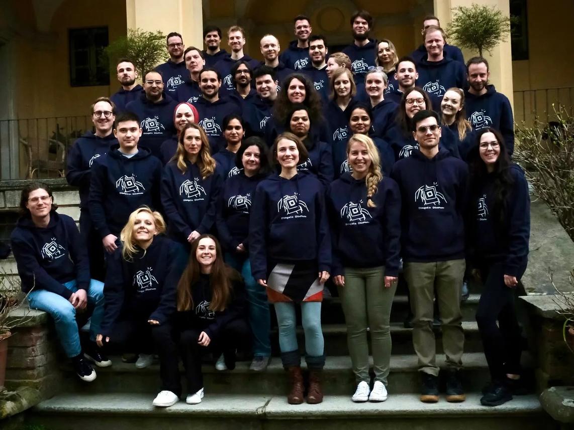 A group of people standing on steps, all wearing matching navy blue hoodies with a logo on the front.