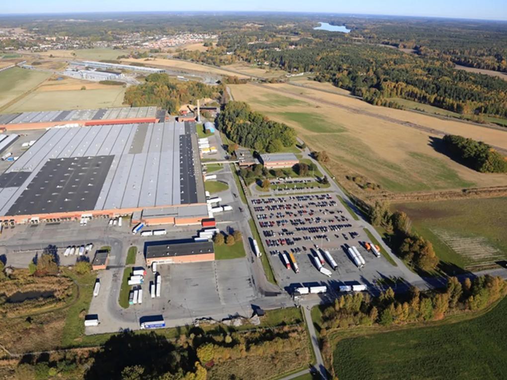 Aerial view of a large industrial warehouse complex with multiple loading docks and a parking area filled with trucks and cars.