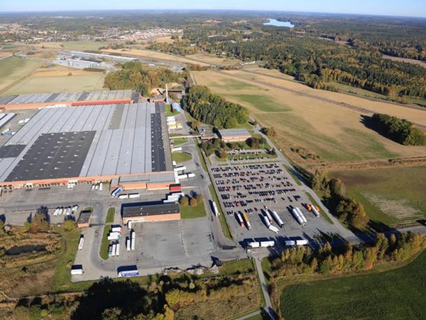Aerial view of a large industrial warehouse complex with multiple loading docks and a parking area filled with trucks and cars.