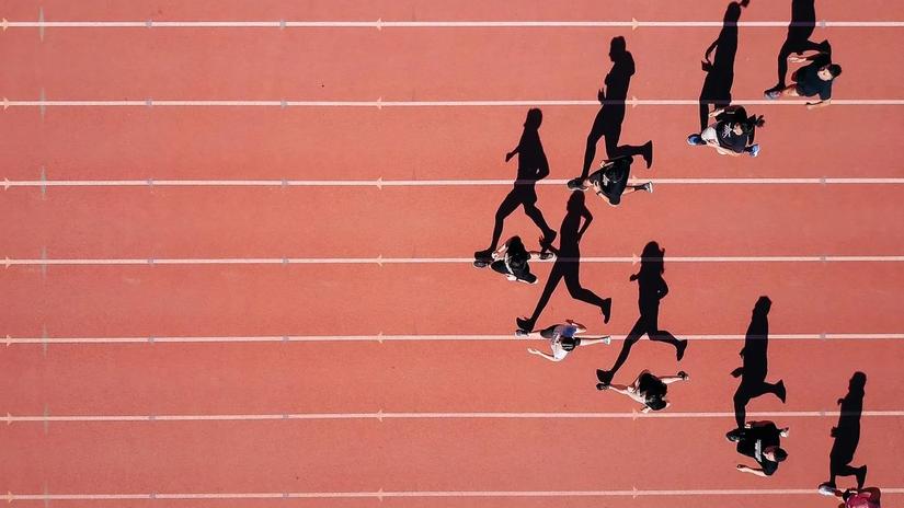 Aerial view of people running on a track, casting long shadows on the surface.