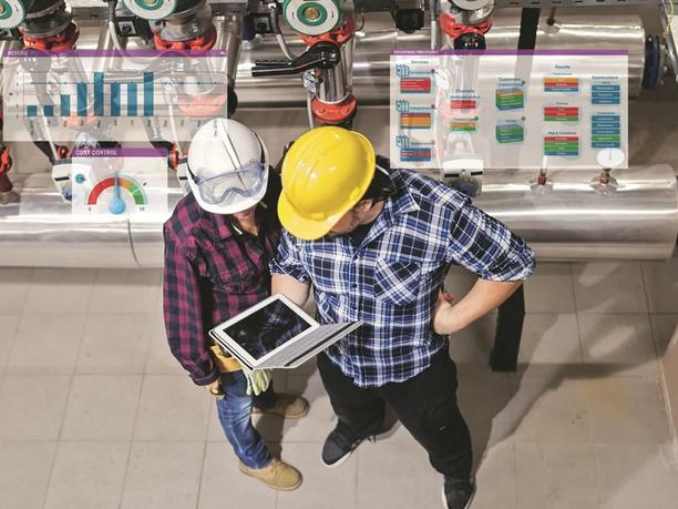 Two workers in hard hats and safety gear are looking at a tablet in an industrial setting.