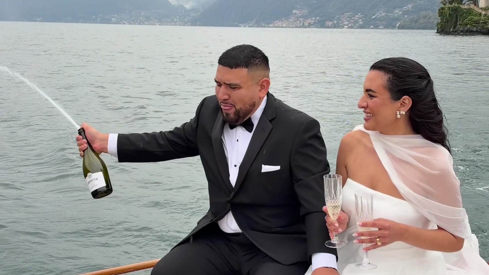 The couple opening champagne on a boat on Lake Como